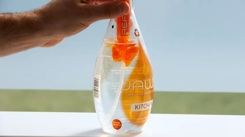JAWS Kitchen Clear bottle with refill pod in neck releasing orange concentrate the bottle.
