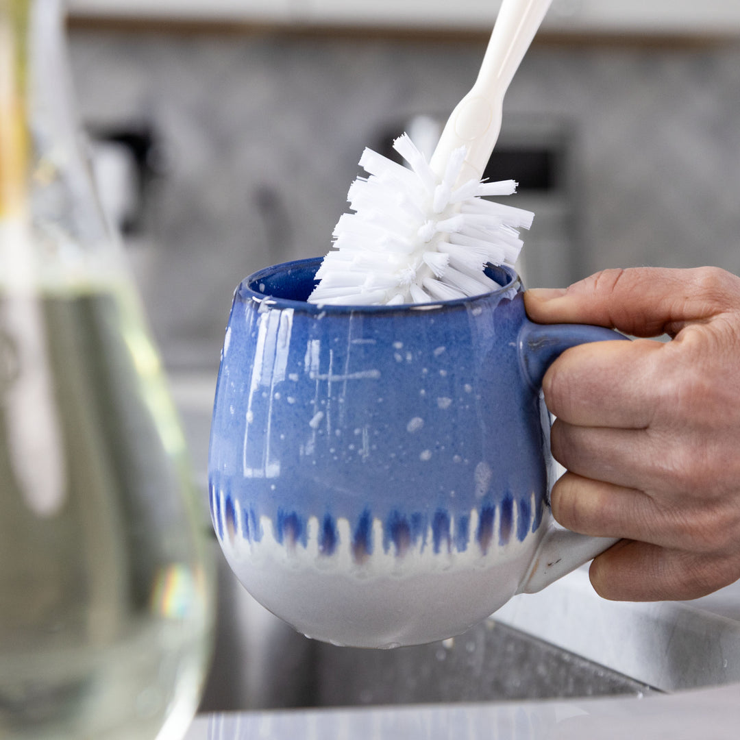 Person cleaning a blue mug with a dish brush in a kitchen setting.