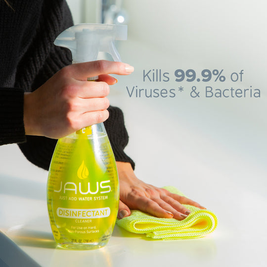 Person holding JAWS Disinfect cleaner and wiping with yellow microfiber.  Text 'kills 99.9% of viruses & bacteria.