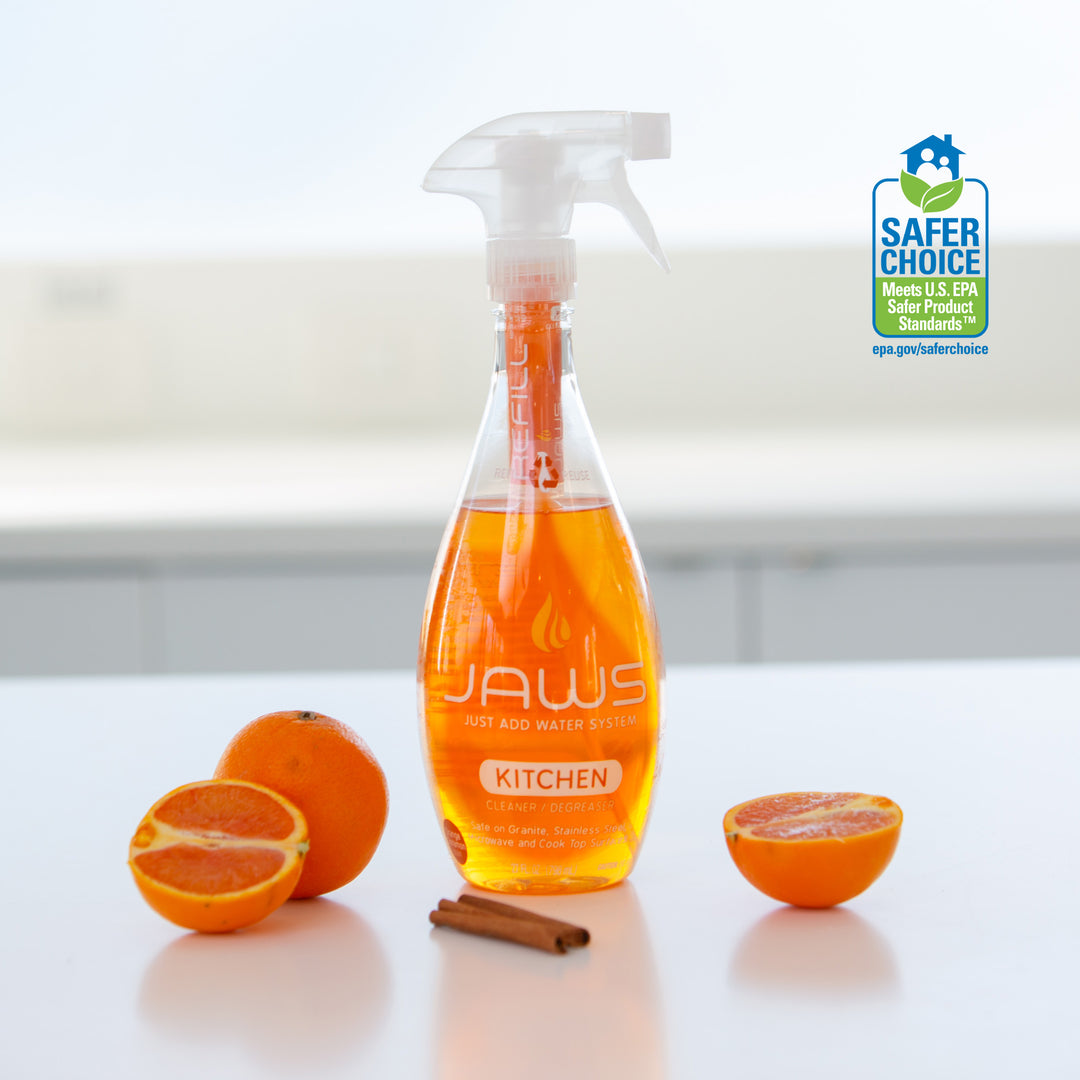 Bottle of JAWS Kitchen Cleaner on reflective surface with orange section and cinnamon next to it.  EPA Safer choice logo in background.