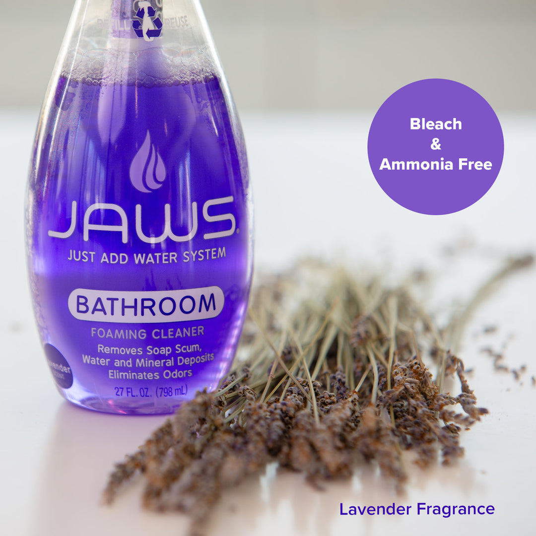 A bottle of JAWS Foaming Bathroom Cleaner with purple liquid, shown next to dried lavender sprigs on a white surface. A purple circular badge reads 'Bleach & Ammonia Free' and 'Lavender Fragrance' is written at the bottom right.
