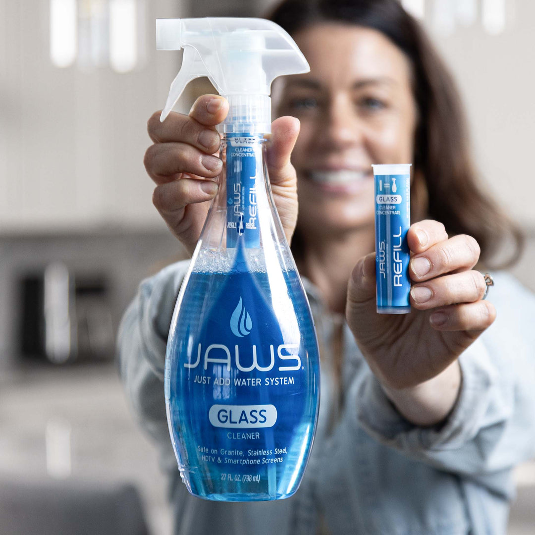 Woman holding a large spray bottle and a smaller refill container of JAWS Glass cleaner.