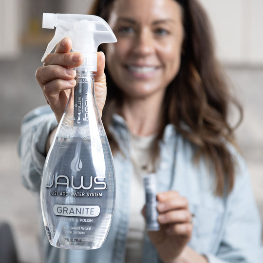 Woman holding a bottle of JAWS Granite cleaner with a JAWS refill pod in her other hand.