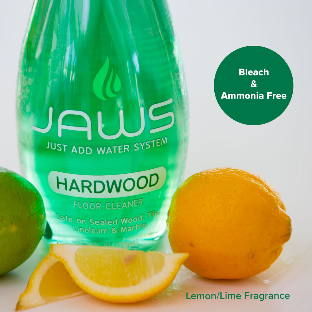 A bottle of JAWS Hardwood floor cleaner next to fresh lemons and limes on a white background. A dark green circular badge on the top right reads 'Bleach & Ammonia Free' and text 'Lemon/Lime Fragrance' is printed at the bottom.