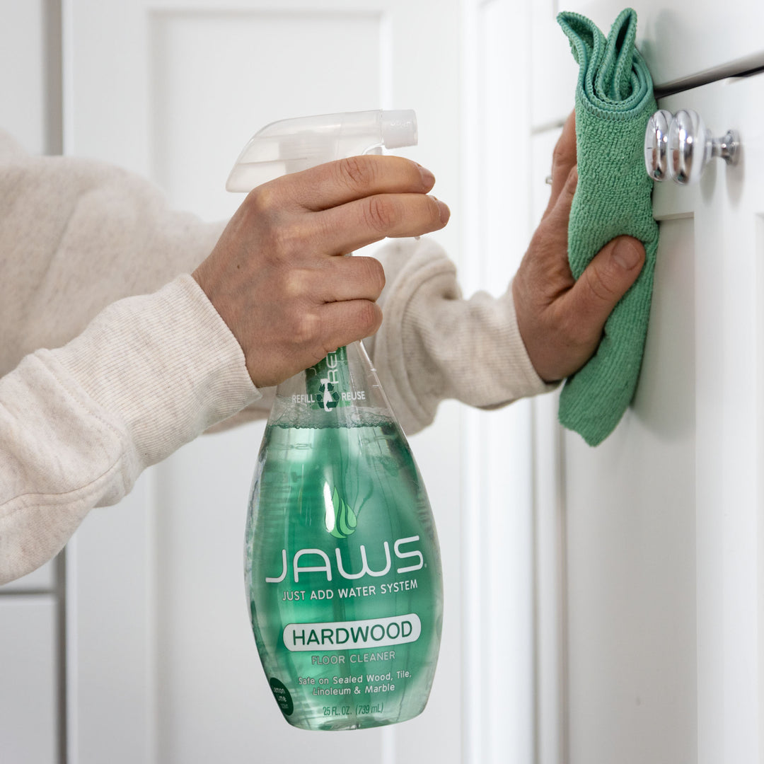 Person cleaning a cabinet with JAWS Hardwood Cleaner and a green microfiber cloth.