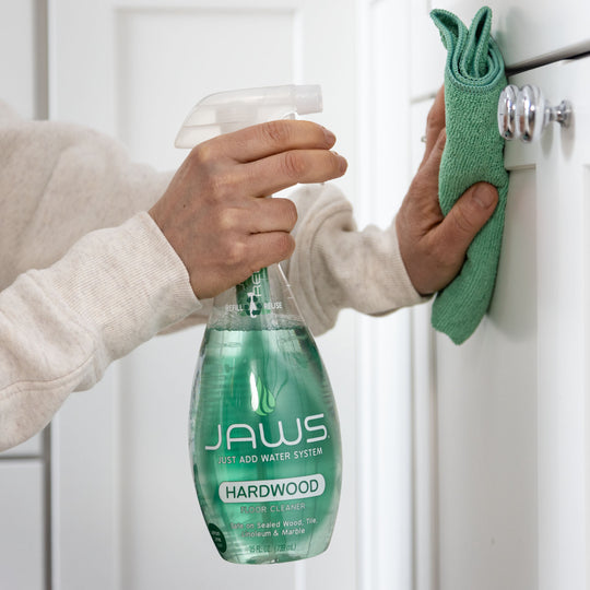 Person cleaning a cabinet with JAWS Hardwood Cleaner and a green microfiber cloth.