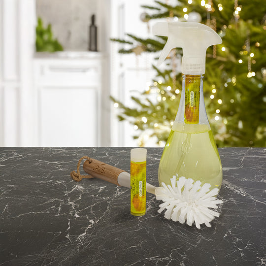 Dish spray bottle, dish brush, and refill pod marble surface with a blurred Christmas tree in the background.