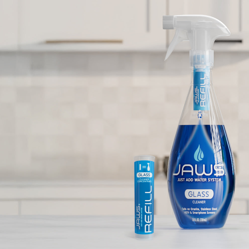 A full bottle of Blue JAWS glass cleaner and one blue JAWS refill pod on a kitchen counter.